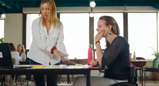 Une femme debout et une femme assise devant un ordinateur sur une table