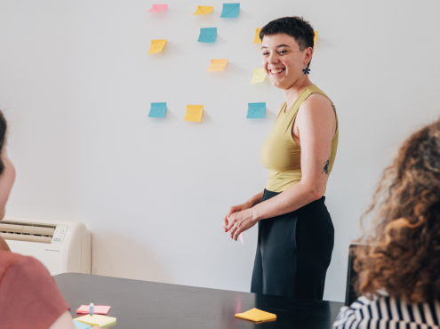 Image de couverture. Photo d'une personne debout qui colle des post it sur un mur en face de 3 personnes assises.