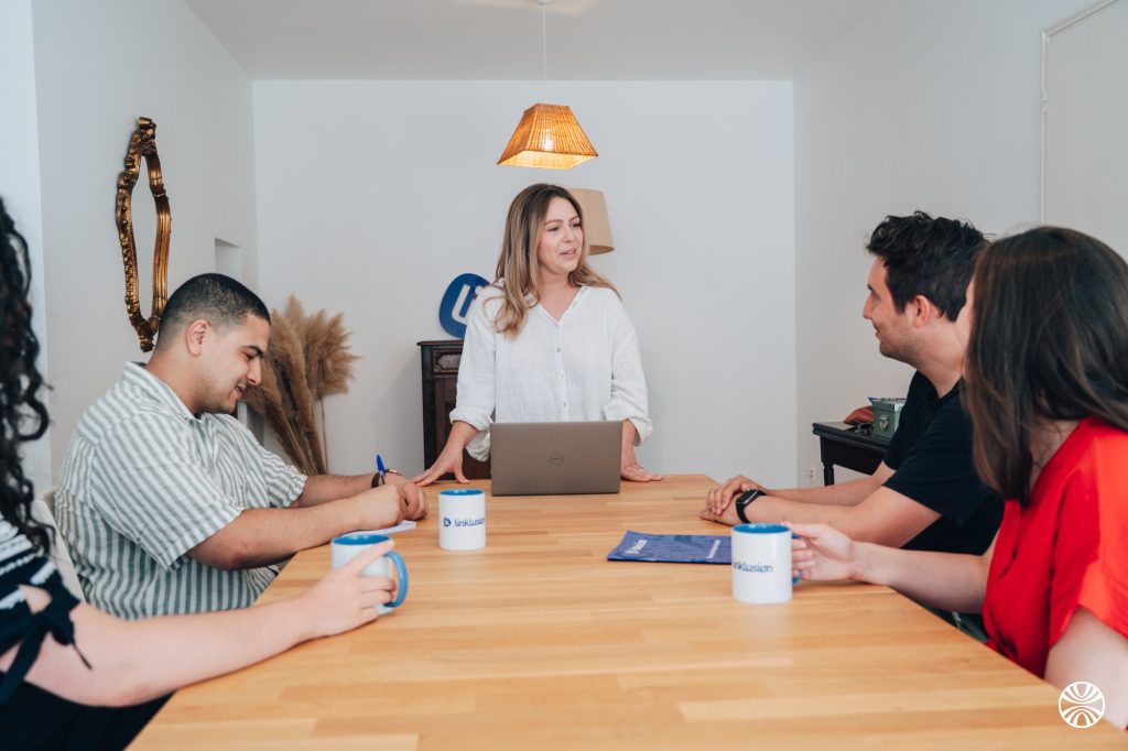 Une personne se tient debout face à plusieurs personnes assises autour d'une table.