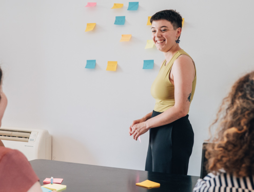 Image de couverture. Photo d'une personne debout qui colle des post it sur un mur en face de 3 personnes assises.